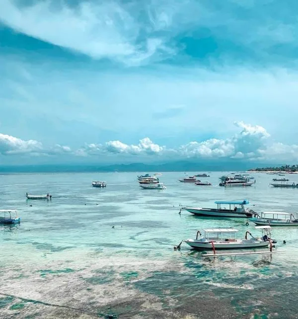Several small motorboats anchored and bobbing in shallow turquoise water off Nusa Lembongan under a bright blue sky.