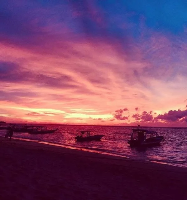 Boats moored along the shore at Nusa Lembongan as a vivid pink and purple sunset reflects on the sea.